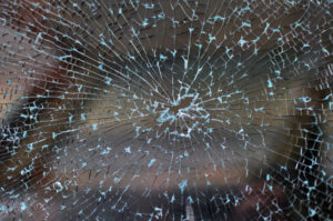 Broken car window with cracked glass pattern and a bullet hole in the middle.