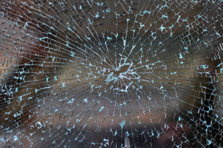 Broken car window with cracked glass pattern and a bullet hole in the middle.